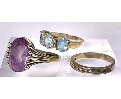 Three gold coloured metal gem-set rings, to include a blue topaz three-stone ring, an amethyst single-stone ring, and a cubic