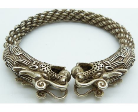 A Chinese white metal bangle depicting dragons and rope twist decoration