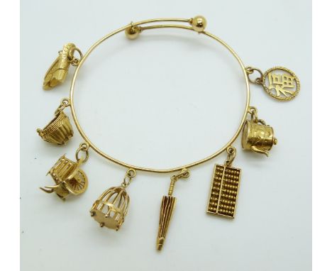 Chinese 20k gold bangle with eight 20k gold charms by Luen Wo including a teapot, abacus, parasol, bird cage, handcart, baske