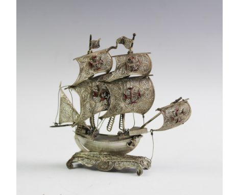 A white metal model of a galleon, designed with filigree sails with red enamel detailing, upon a filigree base with scroll fe