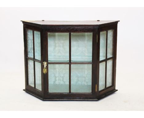 An early 20th century oak hanging wall display cabinet, the angular bowfront cabinet with a single door enclosing a single gl