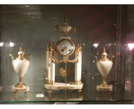 A late 19th century French ormolu and Sienna marble portico clock garniture, the case surmounted by an urn above a floral pai