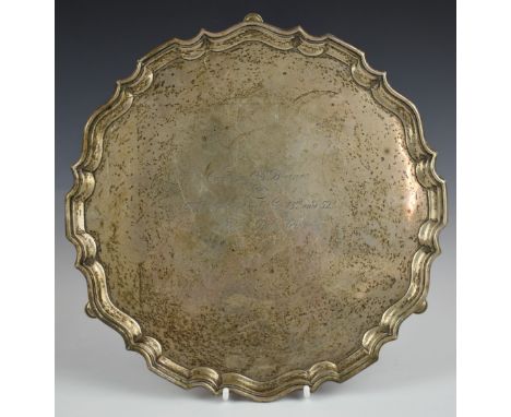 George V hallmarked silver salver with shaped edge, raised on three feet, inscribed to centre to Captain C.S. Baines from the