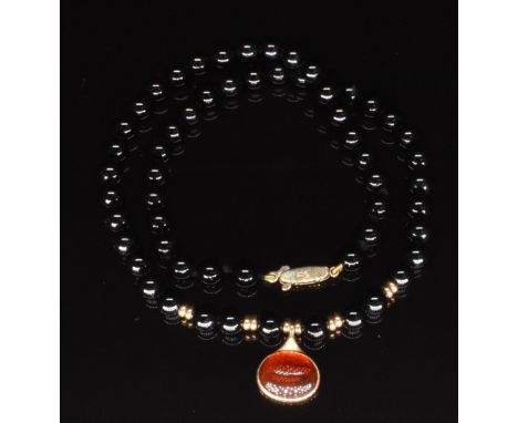 A beaded onyx necklace with a 9ct gold pendant set with a fire opal cabochon and a 9ct gold clasp