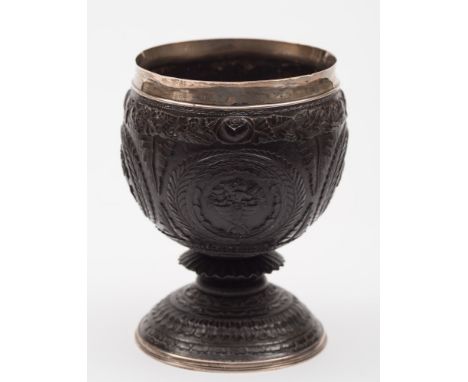 A late Georgian silver mounted coconut cup: with four circular cartouches with monogram, hunting dog and vases of flowers, en