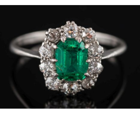 A platinum, emerald and diamond rectangular cluster ring:, the rectangular emerald 6mm x 4mm, within a surround of circular, 