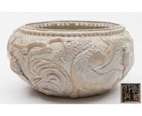 An unusual Chinese cream glazed stoneware bowl: decorated in relief with two horses amongst fruiting trees, foliage and rockw