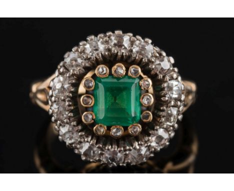 An 18ct gold, emerald and diamond circular cluster ring: with central rectangular emerald approximately 6.2mm long x 5.8mm wi