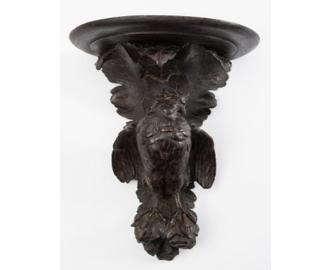 A Black Forest carved wall bracket: the semi-circular shelf mounted on a foliate backplate decorated with bird of prey spread