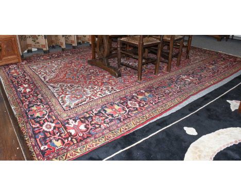 A Heriz Carpet, the raspberry field with flowerhead medallion framed by spandrels and indigo floral borders, 356cm by 252cmBo