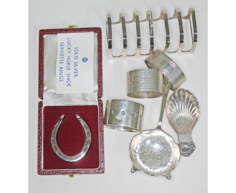 A mixed lot of hallmarked silver comprising three serviette rings, a tea strainer, a Georgian style caddy spoon, a toast rack