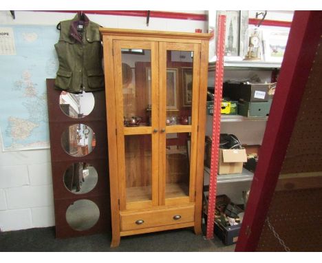 A light oak glazed two door cabinet with single base drawer.  185cm x 90cm x 38cm 