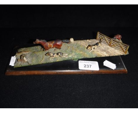 A COLD PAINTED METAL DESK SIZE PAPER CLIP, decorated with a hunting scene, on a wooden base