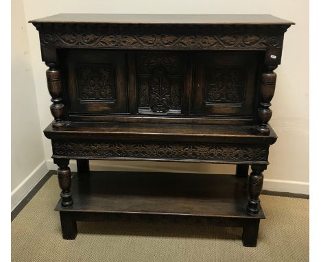 An early to mid 20th Century oak Gothic Revival court cupboard, the plain top over a scrolling foliate carved frieze and cent