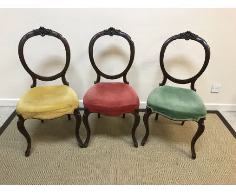 A set of three Victorian mahogany balloon back dining chairs with red, green and yellow velvet upholstered seats respectively