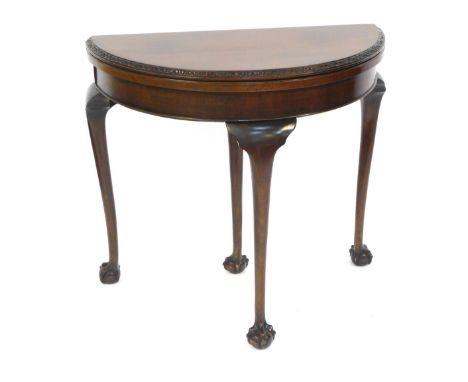 An early 20thC mahogany demi lune card table, topped with a green base lined interior on three ball and claw feet, 74cm high,
