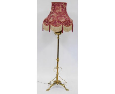 A Victorian brass standard lamp, with a tripod lotus flower base, with scroll bound supports, on claw feet, with red shade, 1
