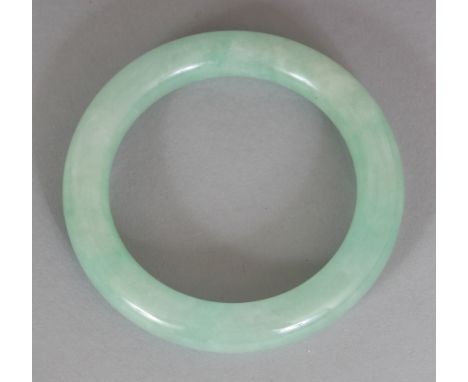A CHINESE CELADON JADE BANGLE, with paler mottled inclusions, 2.8in diameter, the inner rim 2in diameter.