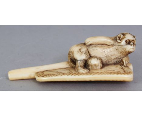 AN UNUSUAL JAPANESE MEIJI PERIOD IVORY NETSUKE, carved in the form of a monkey reclining on a fan, 2.7in long & 0.9in high.