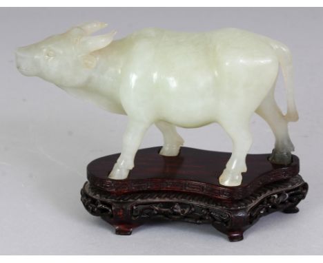 A CHINESE CELADON JADE MODEL OF A STRIDING WATER BUFFALO, together with a fitted wood stand, 4.5in high overall, the jade its