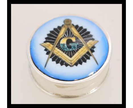 A contemporary silver pill box with an enamel panel featuring a Masonic ecclesiastical design including the letter G.