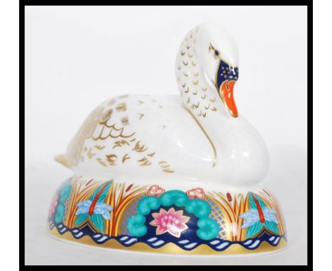 A Royal Crown Derby ceramic paperweight in the form of a nesting swan complete with stopper. Measures 10 cm high and 13.5 cm 