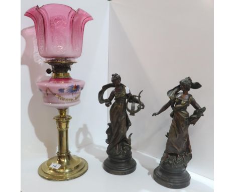 A Victorian oil lamp with cranberry glass shades and milk glass reservoir, together with a pair of French spelter figures of 
