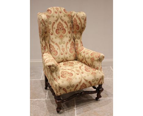 A William and Mary style wing back armchair early 20th century, re-covered in stylised foliate fabric, the camel back extendi