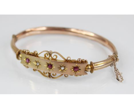 An Edwardian 9ct gold ruby and diamond set hinged bangle, designed as three mixed cut rubies and two rose cut diamonds set to