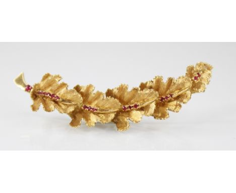 A continental 18ct gold ruby set brooch, modelled as a curved band of five textured oak leaves set with round mixed cut rubie