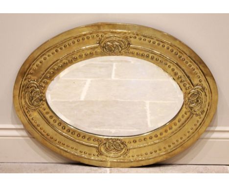 An Art and Crafts brass oval mirror in the manner of Margaret Gilmore, the oval frame embossed with Celtic knot motifs and si