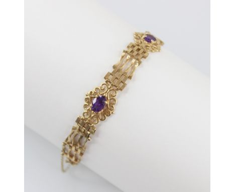 A gold coloured amethyst set bracelet, the gate-link bracelet interspersed by three pierced scrolling panels set with oval mi