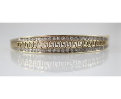 A 9ct gold diamond set hinged bangle, the central channel designed as a pierced greek key border flanked by graduated round b