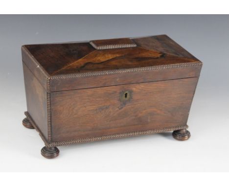 A William IV rosewood tea caddy, of sarcophagus form with gadrooned borders on four bun feet, with hinged cover, the fitted i