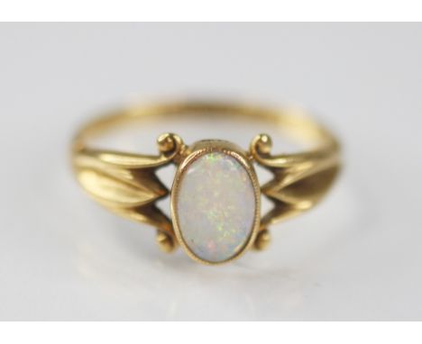 An early 20th century opal 18ct gold ring, the central oval opal cabochon measuring 7.5mm x 5mm, bezel set to pierced scrolli