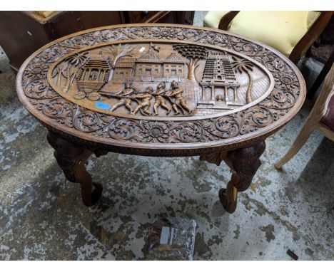 An Anglo-Indian carved wood coffee table, oval top carved in relief with four figures pulling an ornate temple on wheel, with