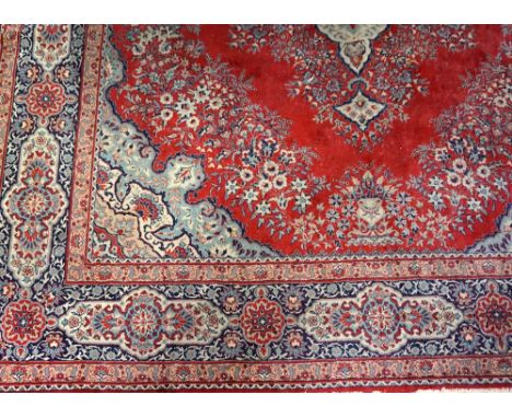 LARGE FLOOR RUGwith a red ground and an ornate central blue medallion encased by a navy and light blue floral border, fringed