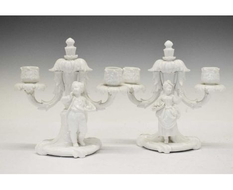 Pair of Continental blanc-de-chine porcelain two-branch figural candelabra in Meissen style, one bearing crossed swords mark,