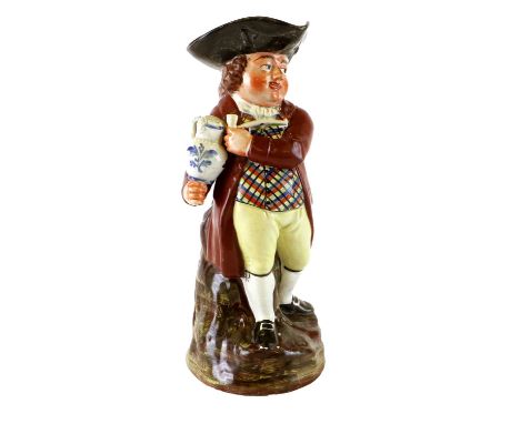 A Walton Pearlware Hearty Goodfellow Toby Jug, early 19th century, modelled with a pipe and balancing a jug of ale upon his f