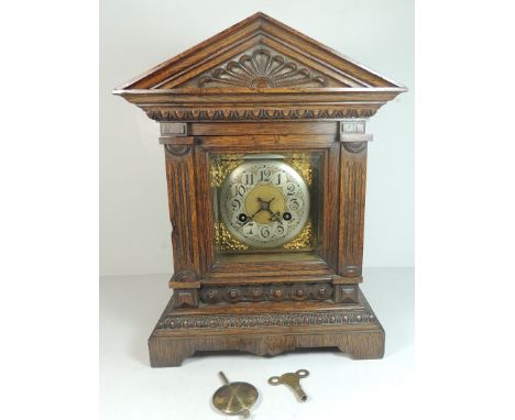 A Junghans mantel clock in architectural oak case having silvered chapter ring with Arabic numerals, gilt scroll spandrels, b