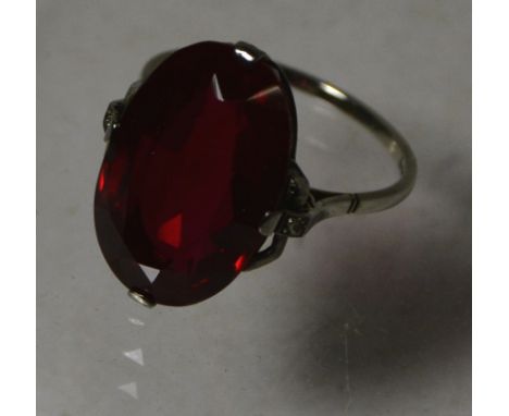 A ladies 18ct white gold Art Deco style ring, set with a large red synthetic garnet and a tiny diamond to each shoulder.  Siz