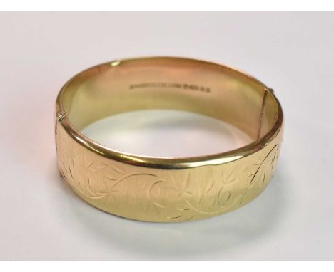 A 9ct yellow gold oval engraved hinged bangle, internal width 57mm, approx 23.2g.