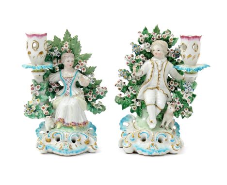 A pair of Derby candlestick figures, c.1765-70, modelled as a boy and girl seated before flowering bocage and holding a small