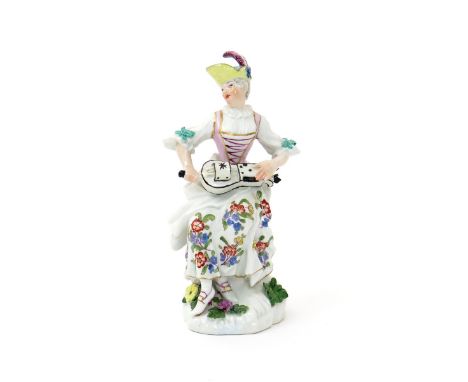 A Meissen figure of Columbine, mid 18th century, seated and playing the hurdy-gurdy, the instrument resting in her lap, weari