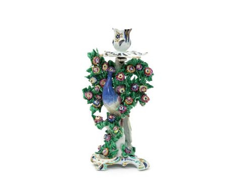 A Bow candlestick figure of a peacock, c.1760, the colourful long-tailed bird perched amidst bold flowering bocage beneath a 