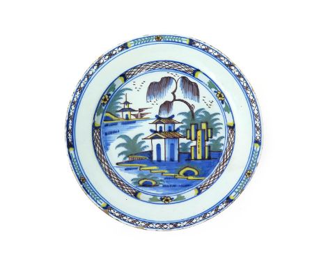 A London delftware charger, c.1770, painted in blue, manganese, green and yellow with a two storey pagoda beneath willow, the