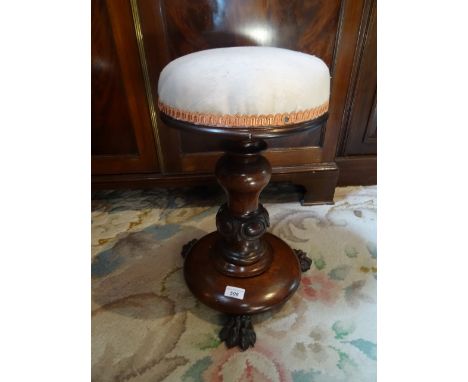 An 18th century mahogany and upholstered piano stool, the central column over circular base on three lion paw feet.