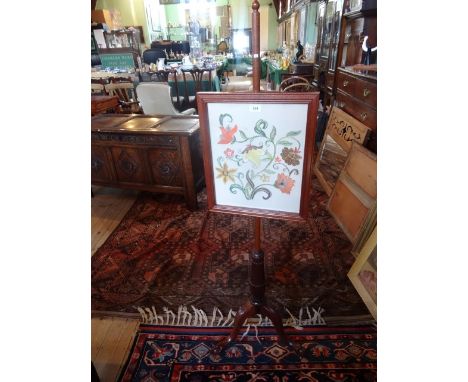 A reproduction pole screen with cross stitch panel over tripod base.