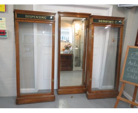 An early 20th century light oak chemists dispensing cabinets having a central mirror flanked by glazed cabinets with gold let
