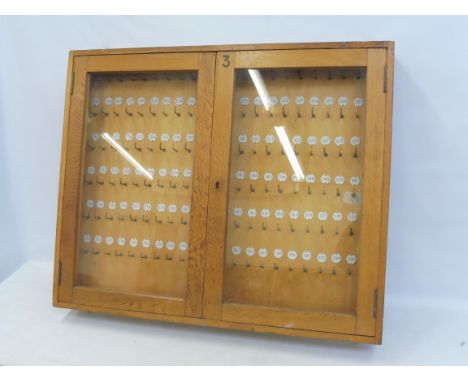 A light oak wall mounted key cabinet, filled with hooks for keys and adjacent numbers, 35 1/2" w x 29" h x 4 1/4" d.